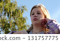 young woman sits under a clear blue sky with tears in her eyes, sunlight gently touching her face. The image conveys deep emotions and the power of vulnerability in a natural setting. 131757775