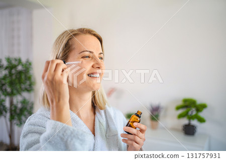 Smiling woman applying essential oil on her face at home 131757931