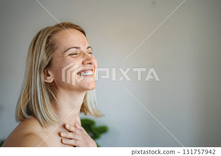 Happy blonde woman laughing with closed eyes and hand on chest 131757942