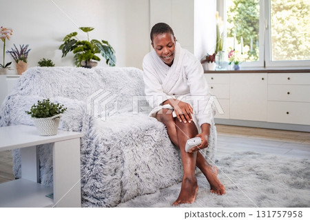 Young woman removing leg hair with an electric epilator at home 131757958