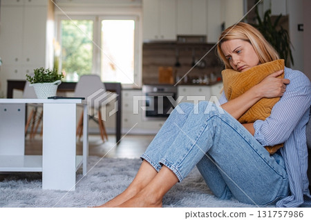 Sad woman sitting on the floor hugging a pillow in her living room Sad woman sitting on the floor hugging a pillow in her living room 131757986