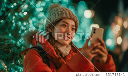 A woman taking a photo with her smartphone of Christmas illuminations on a snowy night 131758141