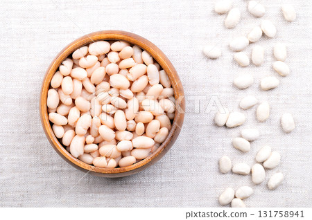 Cooked white beans, in a wooden bowl on linen. Boiled and canned cannellini beans. Preserved white kidney beans. Variety of the common bean, Phaseolus vulgaris, and vegetarian staple food. Food photo. 131758941