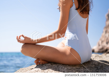 Meditation, yoga, tranquility. Woman meditating on a rock by the ocean with blue sky copy space 131759006