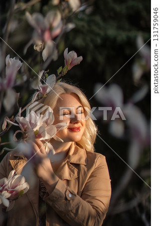 A woman is holding a magnolia flower in her hand and standing in front of a tree. Concept of serenity and beauty, as the woman is surrounded by nature and the flower adds a touch of color. A woman is holding a magnolia flower in her hand and standing in front of a tree. Concept of serenity and beauty, as the woman is surrounded by nature and the flower adds a touch of color. 131759046