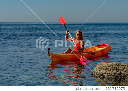 Woman, kayak, paddling a bright orange boat in the clear blue sea, enjoying summer vacation Woman, kayak, paddling a bright orange boat in the clear blue sea, enjoying summer vacation 131759075