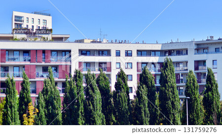 A residential building by lush green trees and surrounded by fresh vegetation on a clear sunny day. Modern architecture residential apartment building complex surrounded by greenery. A residential building by lush green trees and surrounded by fresh vegetation on a clear sunny day. Modern architecture residential apartment building complex surrounded by greenery. 131759276