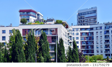 A residential building by lush green trees and surrounded by fresh vegetation on a clear sunny day. Modern architecture residential apartment building complex surrounded by greenery. A residential building by lush green trees and surrounded by fresh vegetation on a clear sunny day. Modern architecture residential apartment building complex surrounded by greenery. 131759279