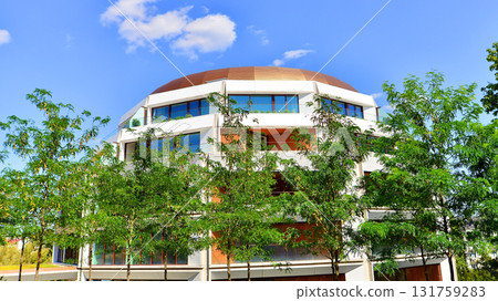 A residential building  by lush green trees and surrounded by  fresh vegetation on a clear sunny day. Modern architecture residential apartment building complex surrounded by greenery. 131759283