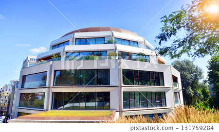 A residential building by lush green trees and surrounded by fresh vegetation on a clear sunny day. Modern architecture residential apartment building complex surrounded by greenery. A residential building by lush green trees and surrounded by fresh vegetation on a clear sunny day. Modern architecture residential apartment building complex surrounded by greenery. 131759284
