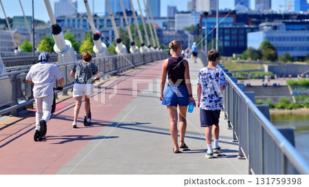 Warsaw, Poland. 15 August 2025. Woman with a child crossing  Swietokrzyski Bridge. Electric scooter users ride along the bike path. Warsaw, Poland. 15 August 2025. Woman with a child crossing  Swietokrzyski Bridge. Electric scooter users ride along the bike path. 131759398