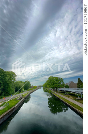 A Beautiful and Serene Canal Reflection Beneath a Dramatic and Cloudy Sky Landscape 131759967