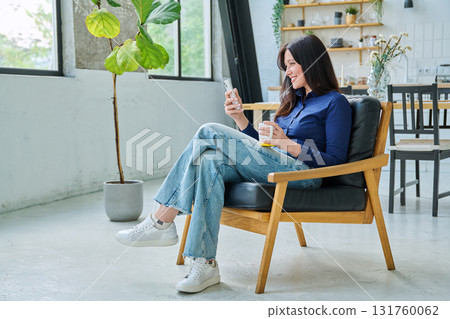 Young happy woman sitting at home in chair using a smartphone 131760062