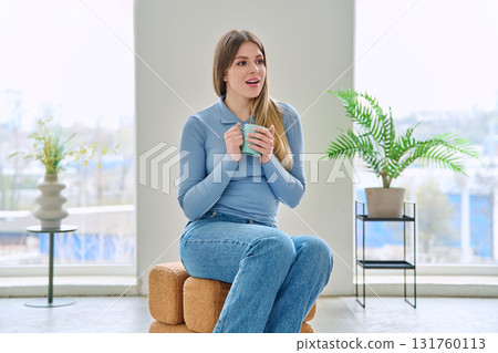 Portrait of relaxed beautiful young woman sitting at home on chair with cup Portrait of relaxed beautiful young woman sitting at home on chair with cup 131760113