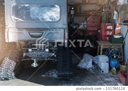 Back POV close-up detail view quad tracked ATV bike offroad vehicle parked front house garage open door on sunny snowy cold winter day. ATV adventure extreme sport. Scoop snow removal tool equipment Back POV close-up detail view quad tracked ATV bike offroad vehicle parked front house garage open door on sunny snowy cold winter day. ATV adventure extreme sport. Scoop snow removal tool equipment 131760128