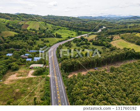 Aerial drone view of Highway winding through lush green mountains between Nan, Thailand. A scenic landscape of the road surrounded by tropical forest and a peaceful countryside Aerial drone view of Highway winding through lush green mountains between Nan, Thailand. A scenic landscape of the road surrounded by tropical forest and a peaceful countryside 131760192