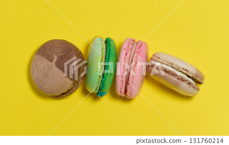 Colorful macarons are laid out in a row on a bright yellow background. Top view. 131760214