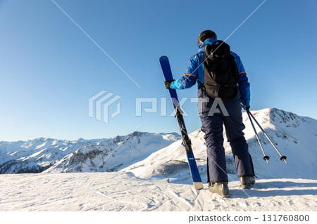 Skier stands on snowy mountain ridge facing bright horizon, ready for descent and challenge. Scene captures spirit of freedom, determination and strength in high alpine wilderness 131760800