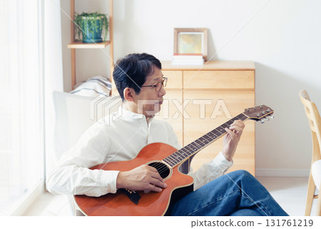 Middle-aged man playing guitar in the living room Middle-aged man playing guitar in the living room 131761219