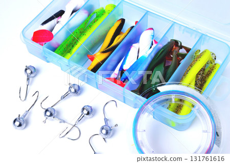 Box for fishing accessories with silicone baits inside, Jig hooks, braided reel on a white background close-up Box for fishing accessories with silicone baits inside, Jig hooks, braided reel on a white background close-up 131761616