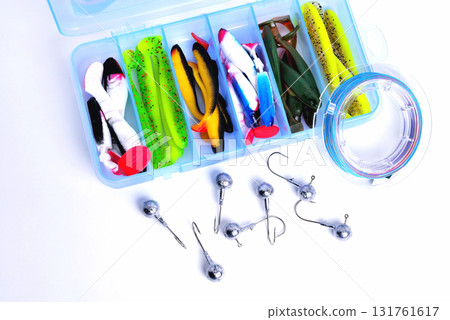 Box for fishing accessories with silicone baits inside, Jig hooks, braided reel on a white background close-up Box for fishing accessories with silicone baits inside, Jig hooks, braided reel on a white background close-up 131761617