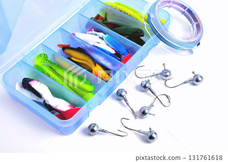Box for fishing accessories with silicone baits inside, Jig hooks, braided reel on a white background close-up 131761618