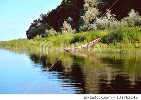 old wooden boat on the river bank close up against the background of green grass and bushes, reflections in the water old wooden boat on the river bank close up against the background of green grass and bushes, reflections in the water 131762149