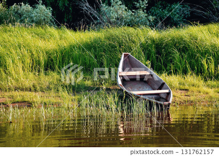 old wooden boat on the river bank or clouds close up against the background of green grass and bushes, reflections in the water old wooden boat on the river bank or clouds close up against the background of green grass and bushes, reflections in the water 131762157