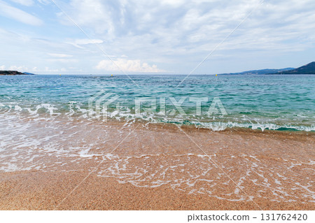 Shore water covers sandy beach of Propriano under cloudy blue sky Shore water covers sandy beach of Propriano under cloudy blue sky 131762420