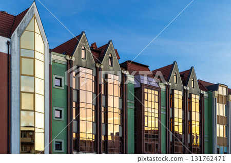 Gdansk, a city on the Baltic coast of northern Poland, Europe. Architectural building with unique exterior details, red roof and gold window, lit by sun, against blue sky at dusk. Exterior perspective 131762471