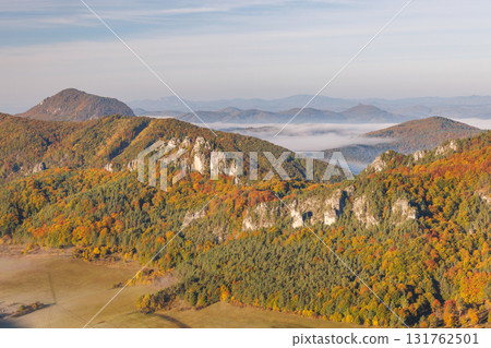 Autumnal hills covered in colorful trees with rock formations and valley fog, against the backdrop of distant mountain ranges. The Sulov Rocks national nature reserve in northwest of Slovakia, Europe. Autumnal hills covered in colorful trees with rock formations and valley fog, against the backdrop of distant mountain ranges. The Sulov Rocks national nature reserve in northwest of Slovakia, Europe. 131762501