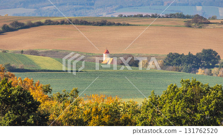 Rural landscape featuring rolling hills, cultivated fields, and a charming building with a red roof under the daylight. Moravia region of Czech Republic, Europe. Rural landscape featuring rolling hills, cultivated fields, and a charming building with a red roof under the daylight. Moravia region of Czech Republic, Europe. 131762520