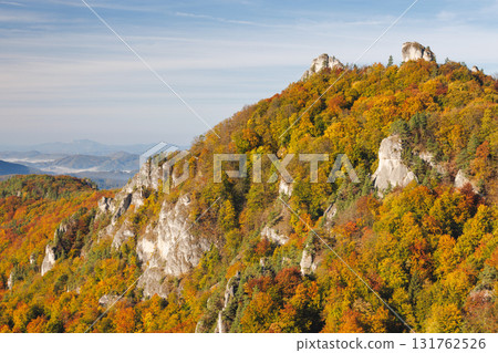 Colorful Autumn Mountain Landscape: Trees display vibrant fall colors on a rocky mountainside against a soft blue sky backdrop. The Sulov Rocks national nature reserve in northwest of Slovakia, Europe Colorful Autumn Mountain Landscape: Trees display vibrant fall colors on a rocky mountainside against a soft blue sky backdrop. The Sulov Rocks national nature reserve in northwest of Slovakia, Europe 131762526