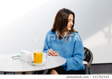 Young woman stirring an orange drink at a table in a cafe 131762543