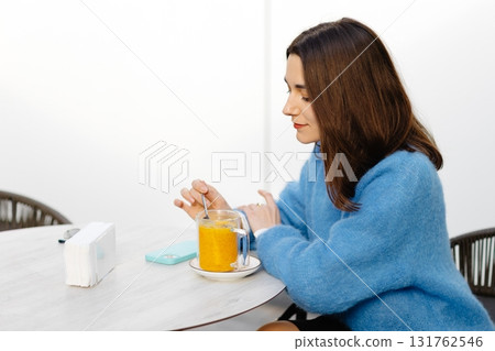 Young woman stirring an orange drink at a table in a cafe Young woman stirring an orange drink at a table in a cafe 131762546
