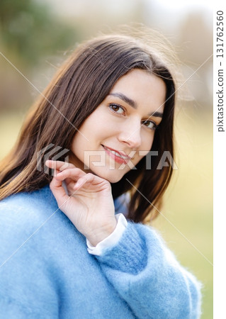 Young woman wearing a blue sweater is holding her chin and smiling 131762560