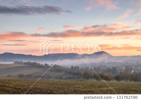 Serene landscape with rolling hills shrouded in mist, painted by a vibrant sunrise sky. Beautiful light 131762590