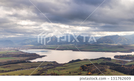 The Liptovska Mara dam in northern Slovakia, Europe. Dramatic mountain landscape featuring a serene lake and expansive cloudy skies. Rolling hills in foreground. 131762609