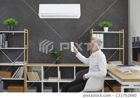Businessman who is sitting on chair in his office switches modern wall air conditioner Businessman who is sitting on chair in his office switches modern wall air conditioner 131762660