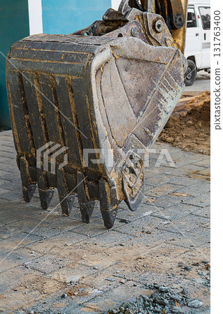 A close-up vertical shot of a steel excavator bucket lowered onto paving slabs at a construction site at the end of a work shift. Attachments of construction specialized equipment A close-up vertical shot of a steel excavator bucket lowered onto paving slabs at a construction site at the end of a work shift. Attachments of construction specialized equipment 131763400