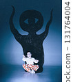 Surreal graphic composition. Little boy making playful scary face before one-eyed monster shadow on blue wall 131764004