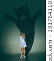 Creative digital artwork. Little girl covering eyes before giant devil shadow on green wall 131764110