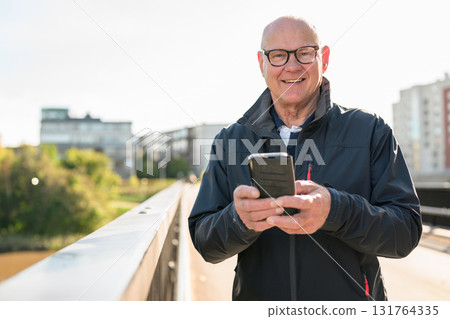 Portrait of senior man using mobile phone while standing on the bridge 131764335