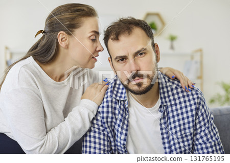 Woman whispering to mans ear at home symbolizing influence, control, or persuasion 131765195