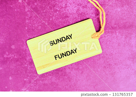 A light yellow tag with SUNDAY FUNDAY on it rests on a textured magenta surface, held by a string, implying a day full of laughter and good times is coming 131765357