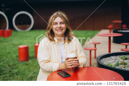 Happy 30s blonde woman enjoying her cup of cappuccino outdoors in cafe, weekend mood. Urban lifestyle concept. 131765428