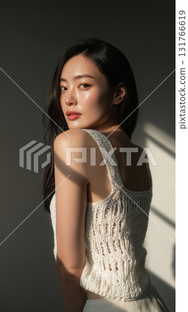 Asian woman poses in cozy knit sweater with soft lighting accentuating her features in a serene indoor setting Asian woman poses in cozy knit sweater with soft lighting accentuating her features in a serene indoor setting 131766619