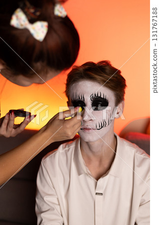 a young guy gets Halloween makeup as a scary skeleton. 131767188