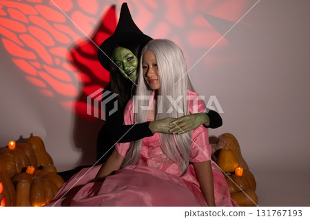 A person in a witch costume is embracing a person with long hair in a pink dress 131767193