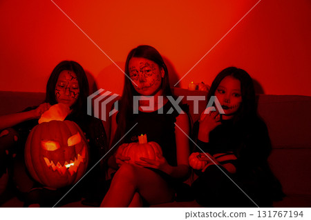 girls are sitting in room,with one of them holding a glowing carved pumpkin 131767194